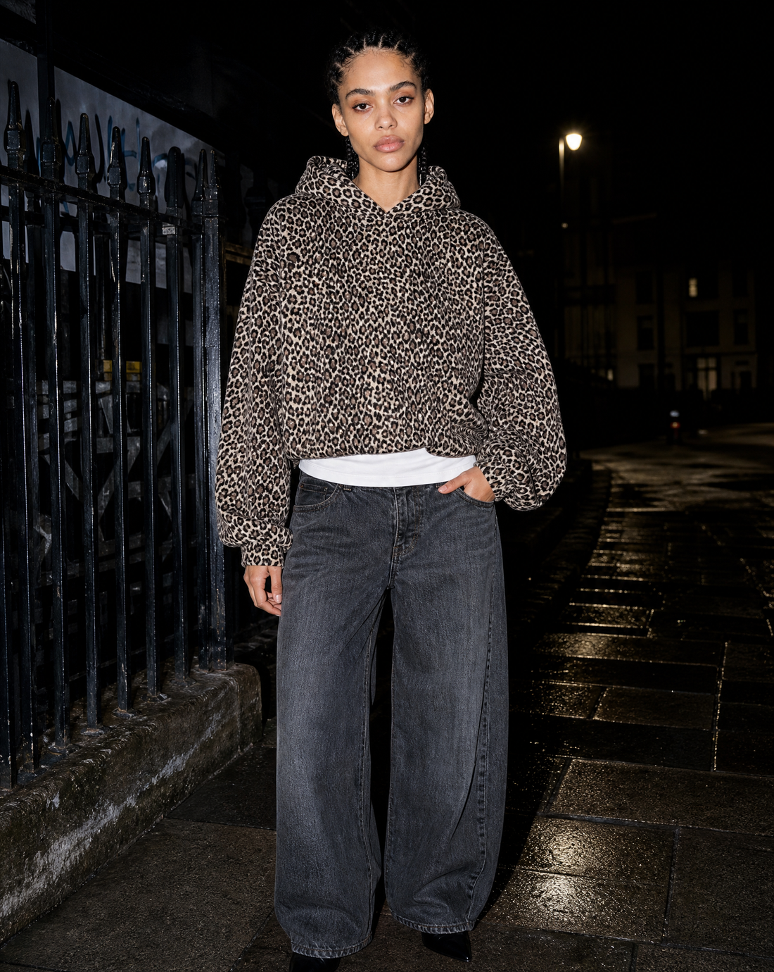 Model in a leopard print hoodie photographed with direct flash beside iron railings at night