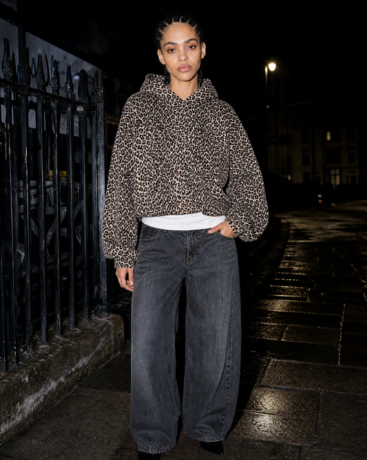 Model in a leopard print hoodie photographed with direct flash beside iron railings at night
