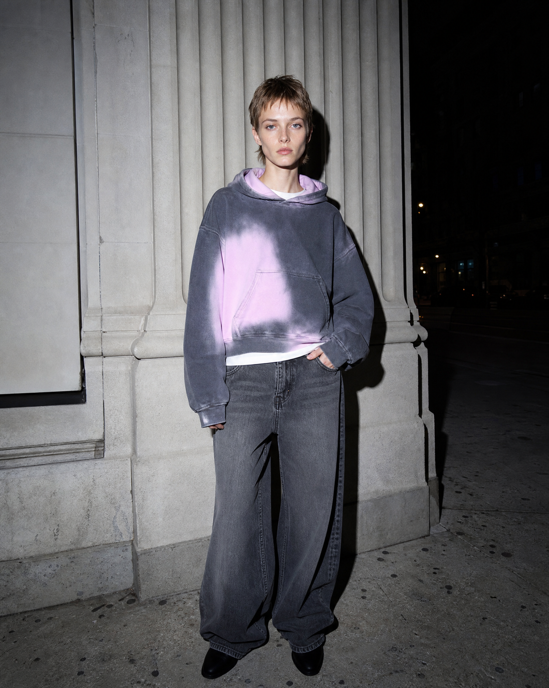 Model in a gradient gothic hoodie lit by direct flash against a pale stone facade at night