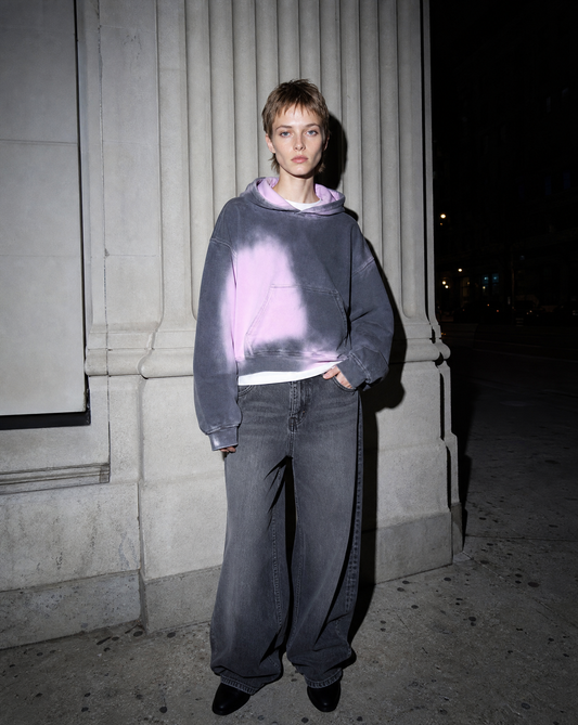 Model in a gradient gothic hoodie lit by direct flash against a pale stone facade at night