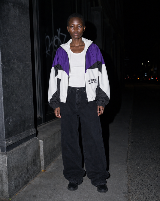 Model in a purple and white colourblock bomber jacket under flash on a dark street