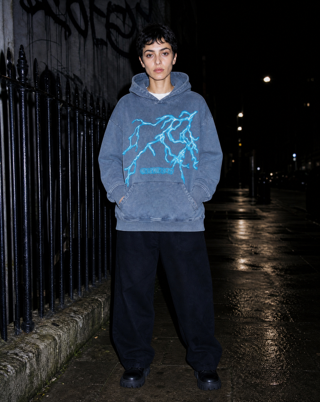 Model in a lightning-print washed hoodie photographed with flash on wet pavement at night