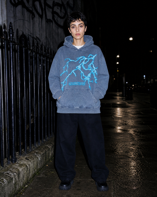 Model in a lightning-print washed hoodie photographed with flash on wet pavement at night